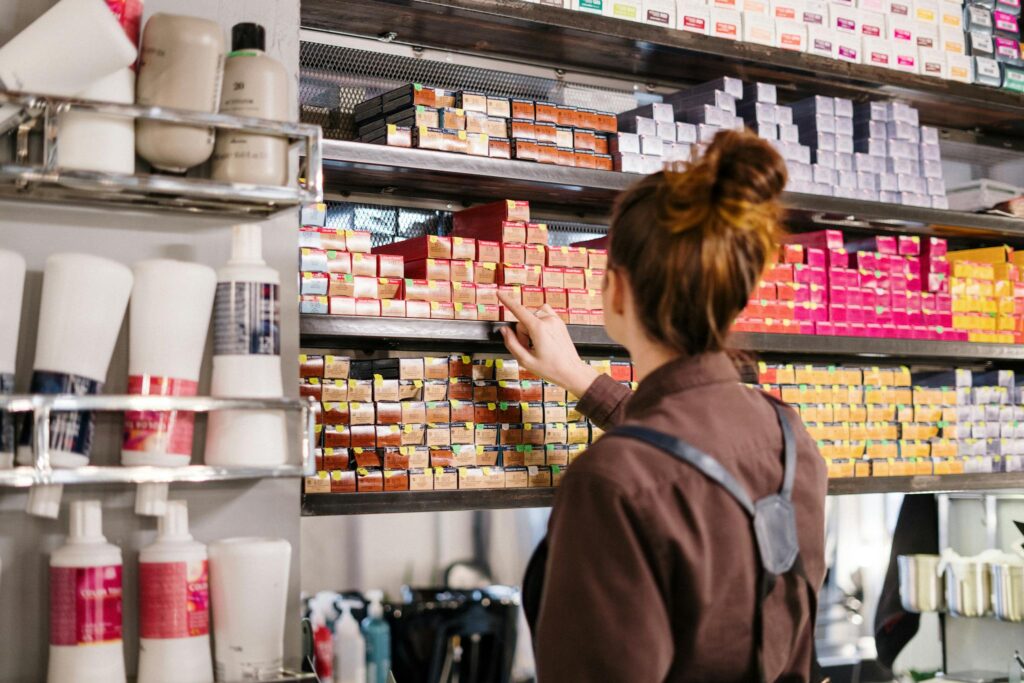 A hairstylist organizing vibrant hair color boxes on a shelf in a beauty salon.