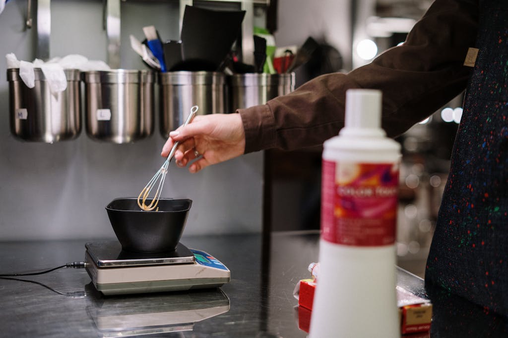 A stylist prepares hair dye with precision using professional tools in a salon setting.