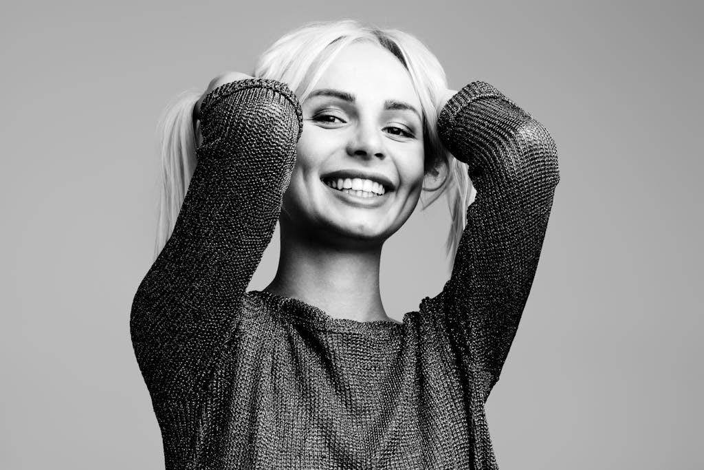 Black and white portrait of a woman smiling joyfully with hands in hair in a studio setting.