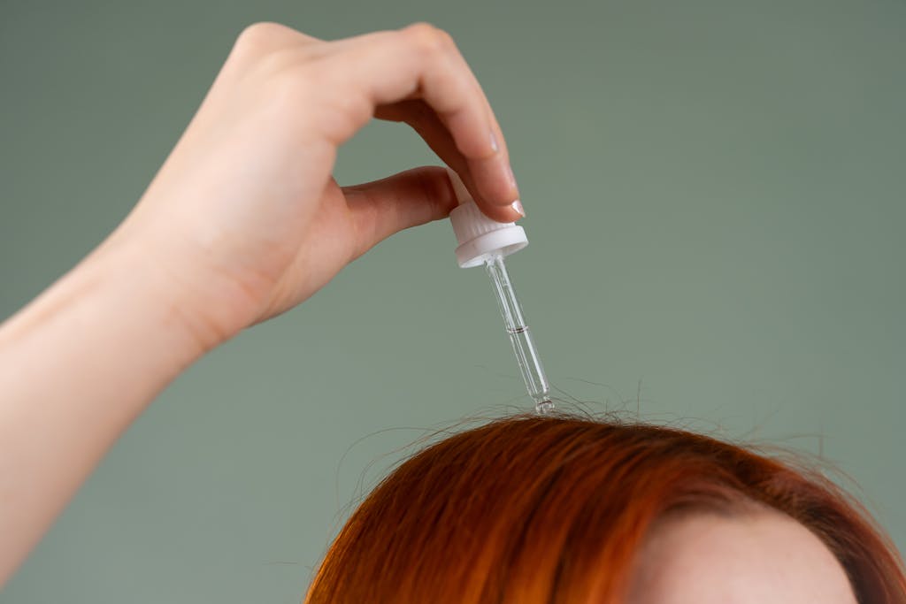 Close-up of hand applying hair serum on red hair with a dropper.